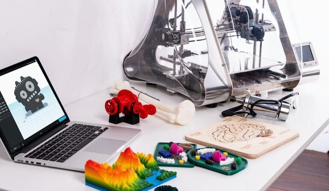 3d printer with printed figures and laptop on the desk